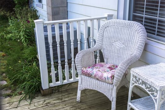 There is a wicker chair with a pillow and a small table in front of the entrance to the house.