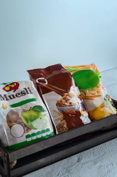 On the table in a wooden container, three packages of muesli in cellophane bags.