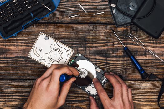 Two Hands with Screwdriver Disassemble HDD. View from above