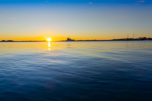 Harbour background at water level of scene of Tauranga harbour with sunrise on horizon blue calm water and sky with golden glow through horizon.