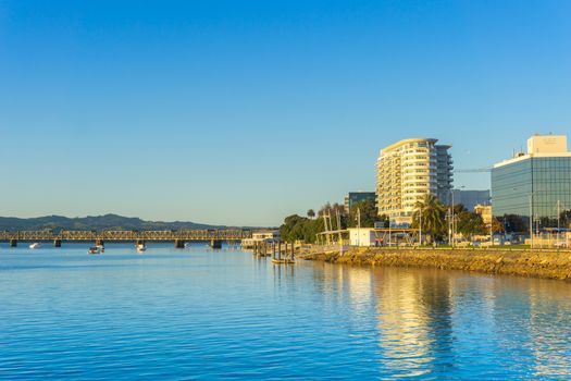 Tauranga waterfront and business district buidlings caught on golden glow of sunrise across idyllic harbor.