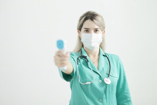 Female doctor or nurse at hospital holds pyrometer in hand. Safety measures against the coronavirus. Prevention Covid-19 healthcare concept. Stethoscope over the neck.
