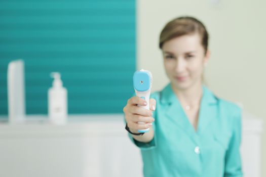 Female doctor or nurse at hospital holds pyrometer in hand. Safety measures against the coronavirus. Prevention Covid-19 healthcare concept. Stethoscope over the neck.