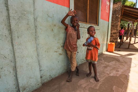 Malindi, Kenya - April 06, 2015:  Two unknown small boys, standing next to wall, smiling and waving to tourist visiting local slum. Many children suffer under poor living conditions in Kenya.