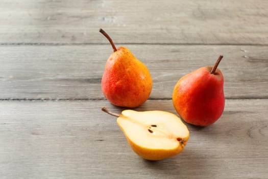 Three ripe pears, one of them cut in half, on gray wooden table.