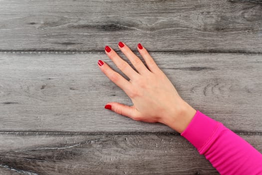 Table top view on young woman right hand with dark red nails on empty gray wood desk.