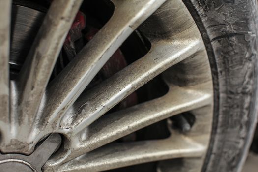 Detail of silver car rim and tire, very dirty from oil and dust.