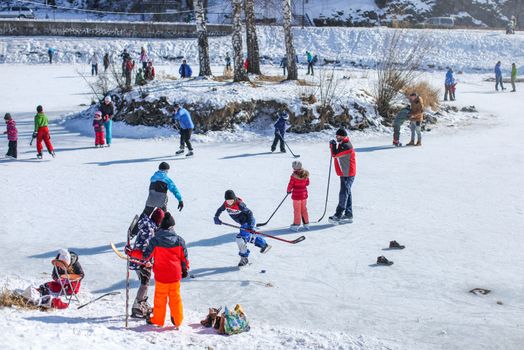 Liptovsky Hradok, Slovakia - March 03, 2018: People of all age groups enjoying sunny day, skating and playing ice hockey on a frozen lake, when temperatures drop on winter.