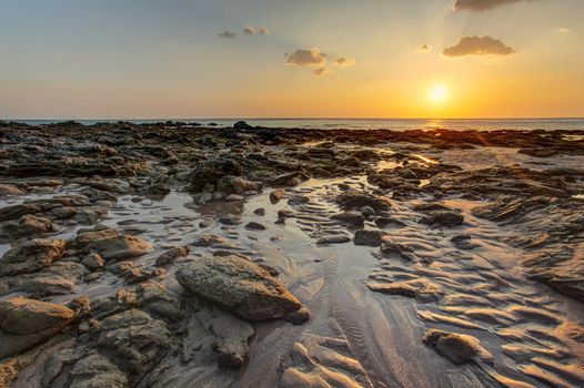 Beach in golden sunset light during low tide showing sand formations and wet stones not covered by the sea. Kantiang Bay, Ko Lanta, Thailand.