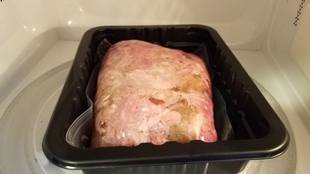 bag of pork meat cooking in container in microwave