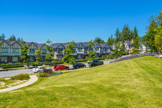 Row of new townhouses with recreation area across the road and parked car on the road