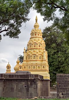 Colorful dome of a small temple with ancient stone wall compound and landscape in village Ambale, Maharashtra, India.