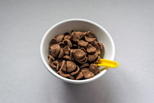 Selective focus image of Wheat & chocolate based cereal flakes in a white bowl with yellow spoon. Food ready to eat.