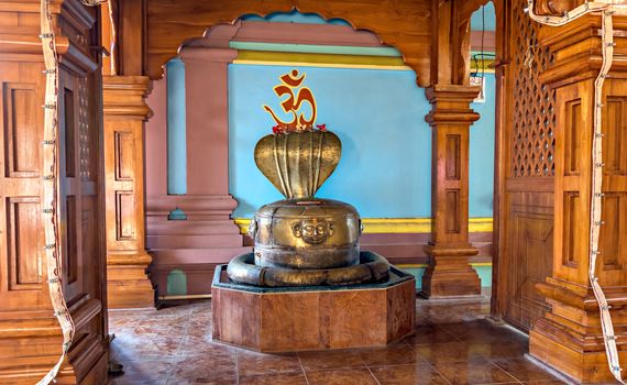 Brass made Hindu religious deities of Shivlingam & Shehnaga in a temple at Velneshwar, Maharashtra. Letter on wall in the back is 'Om' in local language for chanting.