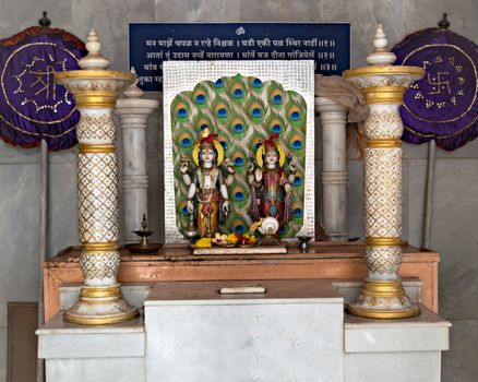 Marble idols of Hindu God Krishna & Goddess Radha with background of peacock feathers at a temple in velneshwar, Maharashtra. Text in the back in regional Marathi language is a religious mantra for chanting all the time.