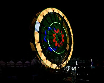 Slow shutter, creative concept photograph of fun fair Giant Ferris wheel spinning at night. Colorful image of lights which can be used as background.