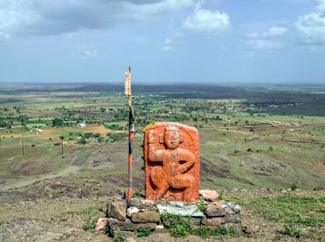 Selective focus, shallow depth of field, Isolated, carved, orange stone idol of Lord Hanuman installed on Dhavalgad with a clear background of nice blue sky.