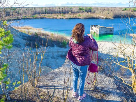 Hiker on mountain top. Woman is standing with an Abandoned Quarry and water on the background. Scenic View Of Land Against Clear Blue Sky. Panoramic View.