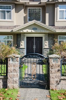 Entrance of luxury residential house with concrete pathway on blue sky background. High end family home with big front yard behind the grid fence