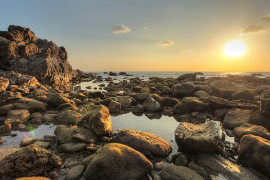 Round rocks and pebbles uncovered in low tide with small sea pools during evening sunset light. Koh Lanta, Thailand