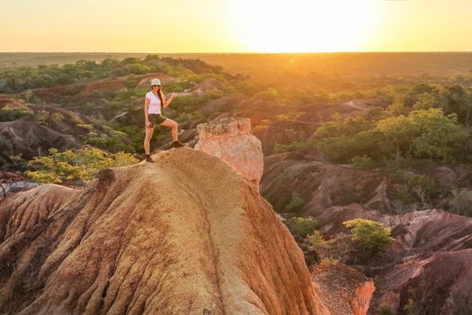 Young woman standing on top of the hill, pointing at the sun during sunset, Marafa (Hell kitchen), Kenya. 