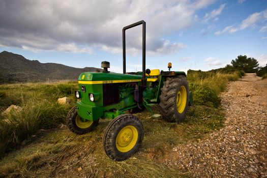 Port de Pollenca, Mallorca, Spain - November 22, 2008: Lonely small green John Deere tractor near hike trail