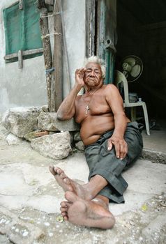 Celestun, Mexico - October 9, 2007: Celestun resident sitting topless on his porch ground on a hot day with emotionless expression in his face.