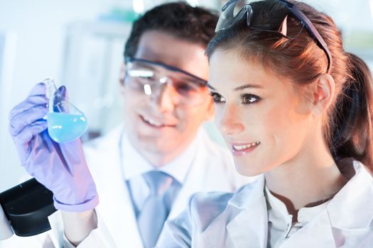 Chemical laboratory. Attractive young PhD student and her post doctoral supervisor scientist observing the blue indicator color shift after the solution destillation.