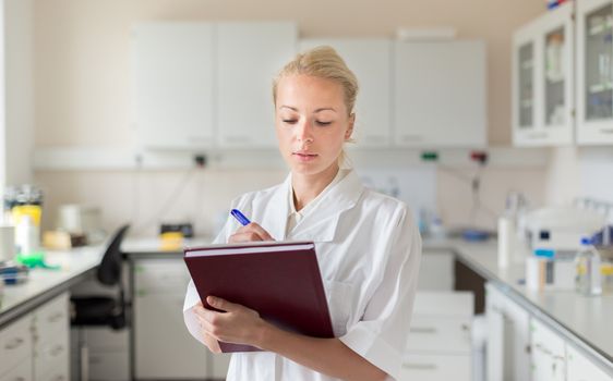 Portrait of young, confident female health care professional taking notes during inventory in scientific laboratory or medical doctors office.