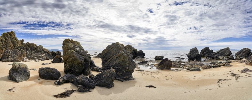 Panoramic view of beach looking out to sea on the West coast of Scotland surrounded by rocks