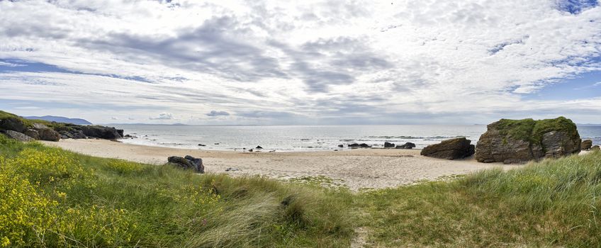 Panoramic view of beach looking out to sea on the West coast of Scotland surrounded by rocks,grass and flowers