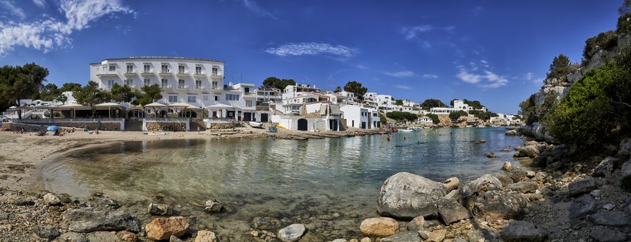 Panorama of beach,houses and small boats moored in the Mediterranean cove of Cala Alcaufar,Menorca,