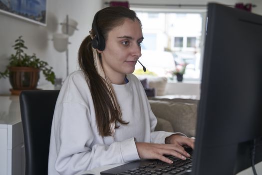 Young girl working from home on computer with headset on