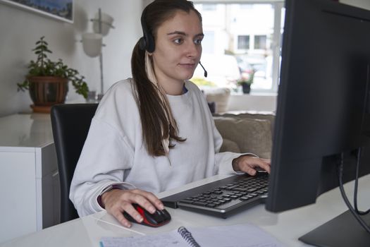 Young girl working from home on computer with headset on