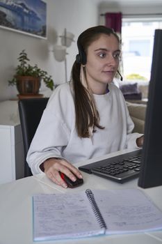 Young girl working from home on computer with headset on