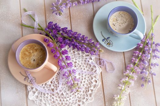 Pink and purple lupine flowers and cup of coffee on a old wooden shabby background