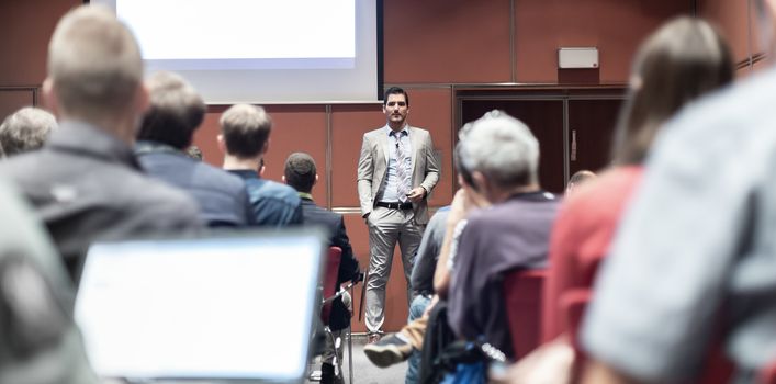 Speaker giving a talk in conference hall at business meeting event. Rear view of unrecognizable people in audience at the conference hall. Business and entrepreneurship concept.