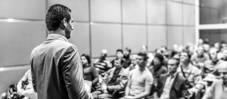 Speaker giving a talk on corporate business conference. Unrecognizable people in audience at conference hall. Business and Entrepreneurship event.