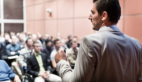 Speaker giving a talk on corporate business conference. Unrecognizable people in audience at conference hall. Business and Entrepreneurship event.