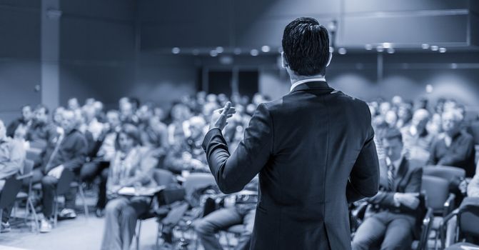 Speaker at Business Conference with Public Presentations. Audience at the conference hall. Entrepreneurship club. Rear view. Panoramic composition. Blue toned greyscale.