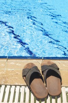 A pair of mens leather sandals by side of swimming pool