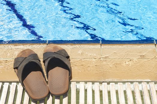 A pair of mens leather sandals by side of swimming pool