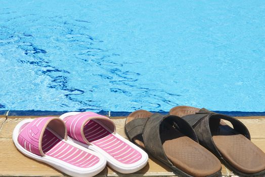 A pair of mens and womans sandals by side of swimming pool