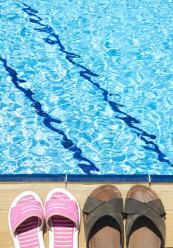 A pair of mens and womans sandals by side of swimming pool