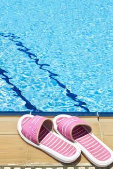 A pair of womens plastic sandals by side of swimming pool