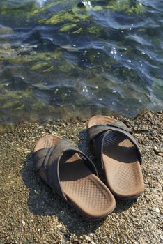 A pair of mens leather sandals on water’s edge by sea
