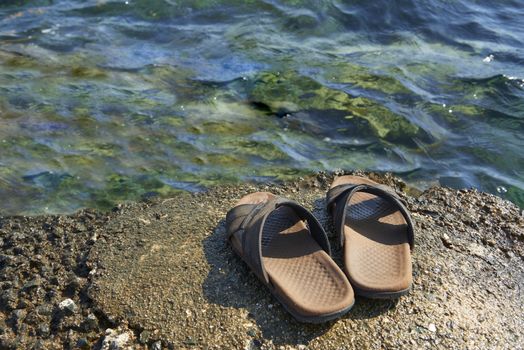 A pair of mens leather sandals on water’s edge by sea