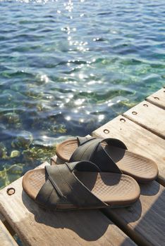 A pair of mens leather sandals on water’s edge by sea