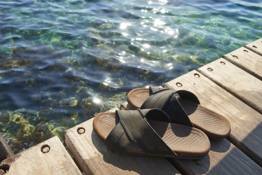 A pair of mens leather sandals on water’s edge by sea