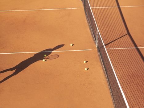 Shadow of tennis player at net with scatttered tennis balls on clay court